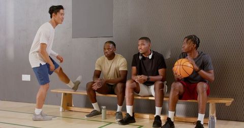 Young athletes sitting on gym bench watching teammate walking in while holding basketball