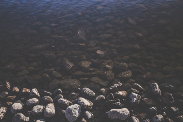 Clear water flowing over smooth stones, ideal for themes of nature, tranquility, and serenity. It can be used for backgrounds in wellness or meditation content, environmental campaigns, outdoor activity promotions, or artistic projects focusing on natural beauty.