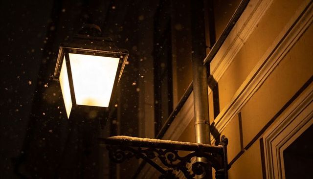 Victorian street lantern casting warm amber light on snowy urban facade at night