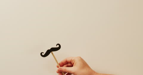 Hand Holding Moustache Prop on Stick with Minimalist Background