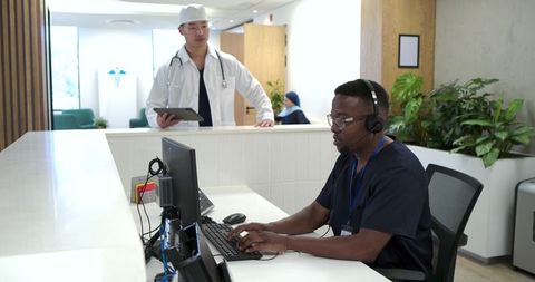 African american clinic receptionist typing at desk wearing headset assisting patients