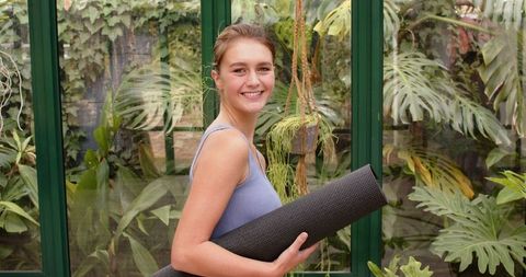 Woman Preparing for Yoga with Mat in Planted Conservatory