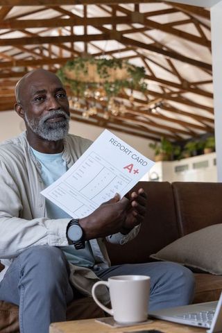 Senior african american man proudly showing a+ report card in cozy living room