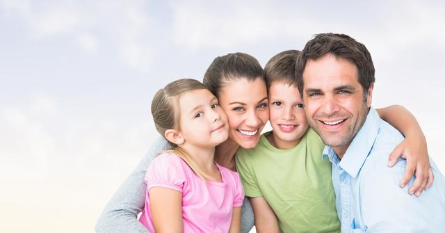Smiling family of four close together with blue sky in background. Ideal for use in advertisements, family-focused promotions, or articles on family and parenting.