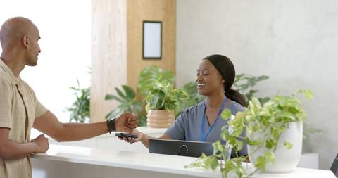 African american clinic receptionist accepting contactless payment from patient smartwatch