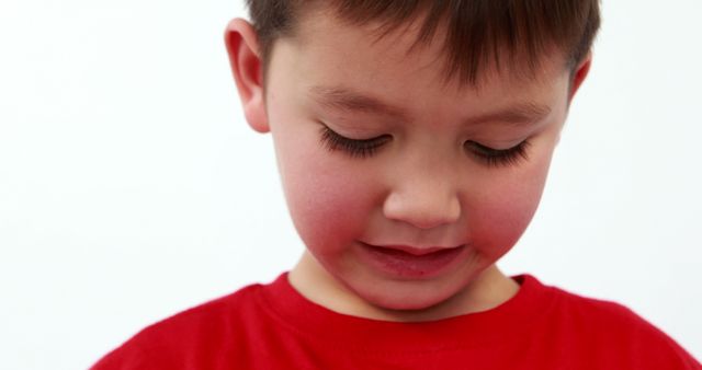 Young boy with brown hair wearing red shirt is looking down thoughtfully. Great for use in educational materials, emotional awareness content, parenting articles, child psychology resources, and family-oriented advertisements.