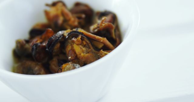 Close-up of marinated mushrooms served in a white ceramic bowl, focusing on the texture and seasoning of the food. Ideal for use in culinary websites, recipe blogs, healthy eating articles, and promotional material for restaurants. The minimalist background highlights the gourmet delicacy, making it suitable for editorial use or marketing of gourmet products.