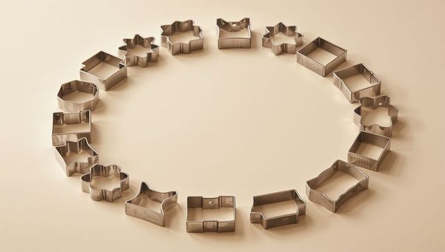 Arranging stainless steel cookie cutters into circular ring on beige tabletop