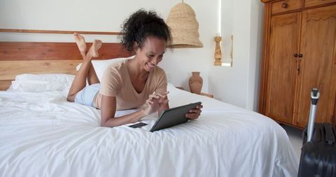 Woman Enjoying Leisure Time on Bed with Tablet in Cozy Bedroom