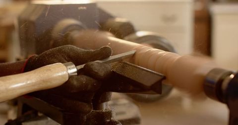 Craftsman shaping wooden cylinder using lathe and chisel in workshop
