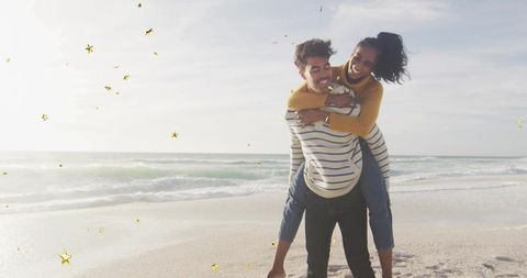 Young couple enjoying piggyback on beach with golden star confetti and ocean copy space