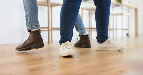 Companions shuffling on hardwood floor wearing canvas sneakers and leather boots