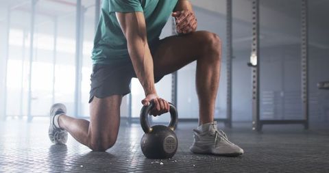 Man Kneeling Lifting Kettlebell in Gym for Strength Training