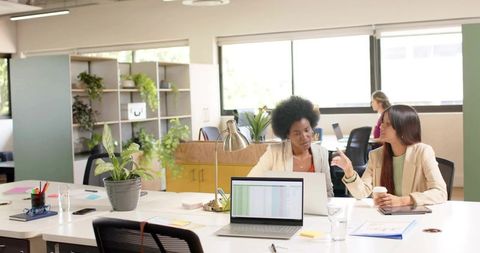 Two colleagues collaborating over spreadsheet on laptop in bright modern open-plan office