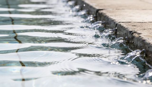 Sunlit pool edge with cascading water droplets, shimmering ripples and weathered concrete rim