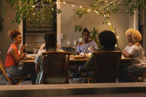Close friends enjoying cozy outdoor dinner under string lights and candles, intimate evening