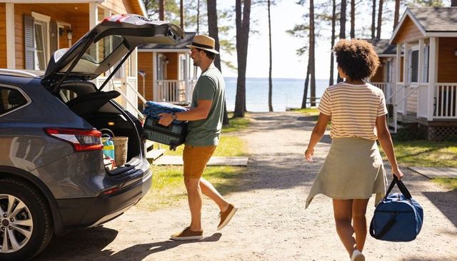 Couple unloading suv at lakeside cabins carrying luggage and crate for summer cottage