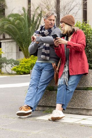 Senior couple checking smartwatch and sharing smartphone on urban plaza planter bench