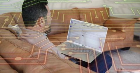 Asian man reading email on laptop while relaxing on tan sofa with tech circuit overlay