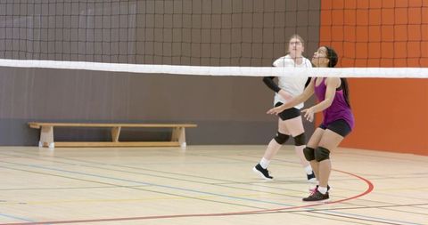 Female volleyball teammates preparing for play on indoor gym court during practice