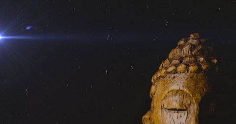Wooden buddha sculpture illuminated at night with raindrops