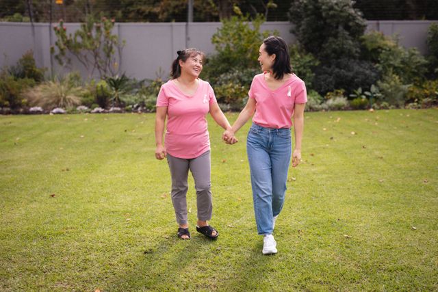 Asian senior woman and her adult daughter are walking hand in hand in a garden, both smiling and enjoying each other's company. This image can be used for promoting family values, senior lifestyle, outdoor activities, and intergenerational bonding. Ideal for websites, brochures, and advertisements focusing on family relationships, health, and wellness.