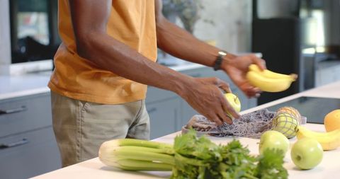 African American man arranging fresh bananas and green apples on modern kitchen island