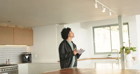 African american man inspecting modern kitchen track lighting while holding tablet at home
