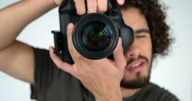 A young Caucasian male photographer focuses a camera lens directly at the viewer, with copy space. His intent gaze and the professional camera suggest a moment captured during a photoshoot or a creative project.