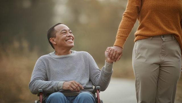 Man in Wheelchair Smiling at Companion on Autumn Pathway