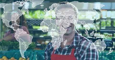 Smiling produce clerk wearing red apron arranging fruit crates with digital world map