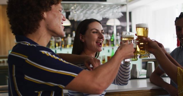 This image features a group of friends toasting and cheering with beer in a modern bar. It captures the essence of socializing and celebrating together in a contemporary setting. This could be used for advertising bars, nightlife, drinking occasions, or articles about social gatherings.