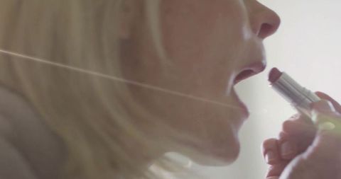 Mature woman applying lipstick in soft backlit closeup, warm tone beauty ritual skincare