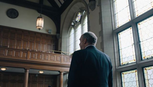 Senior man standing before stained-glass windows in historic chapel interior
