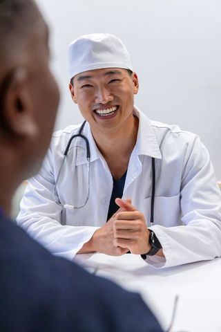 Asian male doctor smiling and consulting african american male patient in clinic visit
