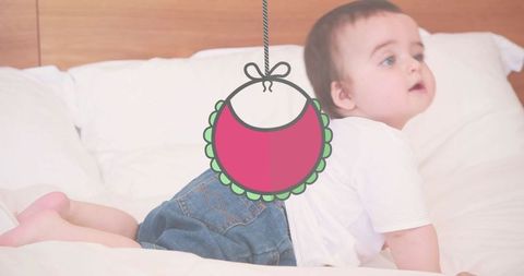 Happy caucasian baby crawling on bed with hanging bib overlay