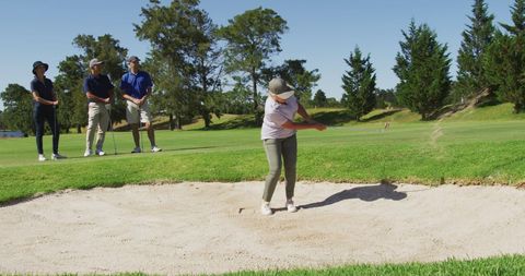 Senior Woman Hits Golf Ball from Sand Trap on Sunny Day
