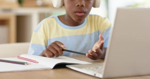 African american boy studying at laptop with headphones and notebook for online learning