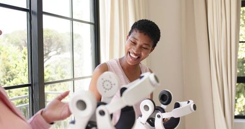 African american woman smiling and inspecting multi-arm robotic therapy device by window