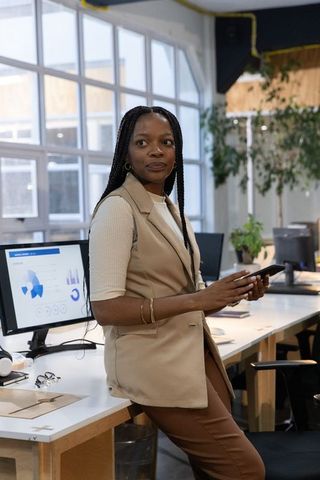 African american businesswoman leaning on desk holding phone reviewing analytics