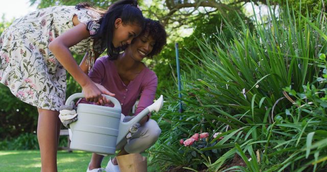 An African American mother and daughter are seen happily tending to plants in their garden. Both are smiling, indicating the joy they find in spending time together outdoors. This is a great representation of family bonding, especially during times of quarantine and lockdown. The image can be used in articles, blogs, or ads related to family life, parenting, nature activities, and staying productive at home during isolation.