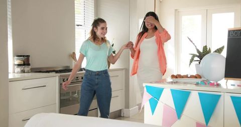 Surprised pregnant woman being led by friend at pastel baby shower in bright kitchen