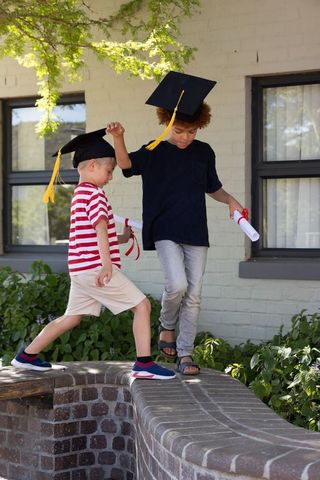 Young graduates balancing on curved brick wall wearing mortarboards and holding diplomas