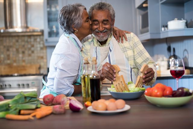 Senior couple enjoying a moment together while preparing food in their kitchen. The scene is filled with fresh vegetables, eggs, and other cooking ingredients, showcasing a healthy and vibrant lifestyle. This image is ideal for use in advertisements, brochures, or articles related to senior living, healthy cooking, and family bonding.