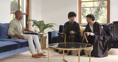 Proud parent observing sons in graduation gowns at home