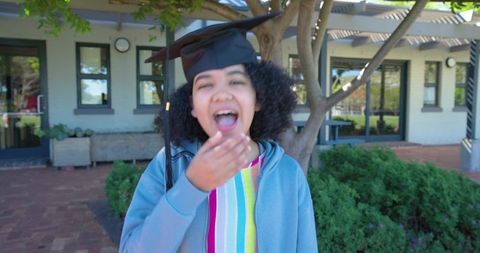 Joyful african american teen graduate laughing with mortarboard on school campus
