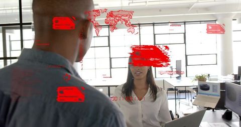 Woman collaborating with colleague using laptop and red HUD data overlays in bright modern office