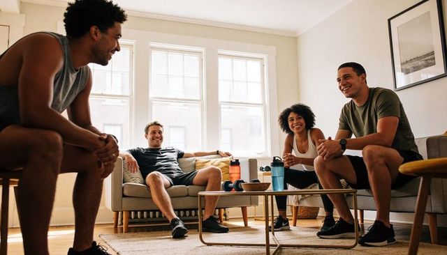 Group of friends in athletic wear chatting and relaxing in sunlit apartment living room