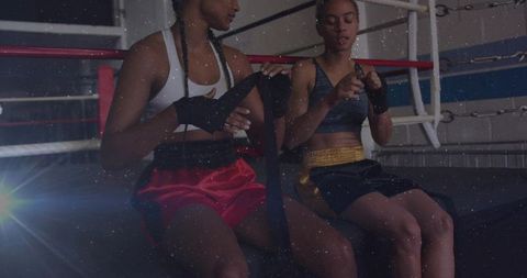 Female boxers wrapping hand wraps on ring apron during training session in boxing gym
