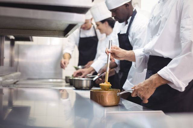 Professional chefs are cooking and preparing food in a restaurant kitchen. This image can be used for articles or advertisements related to culinary arts, restaurant business, teamwork in kitchens, or professional cooking courses. It highlights the collaborative effort and skill involved in a commercial kitchen setting.